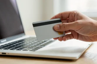 Une main tient une carte bancaire devant un ordinateur portable